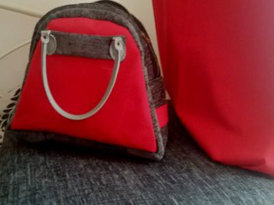 Red and Grey Hand Bag against Grey Sofa Seat Cushion and Red Curtain